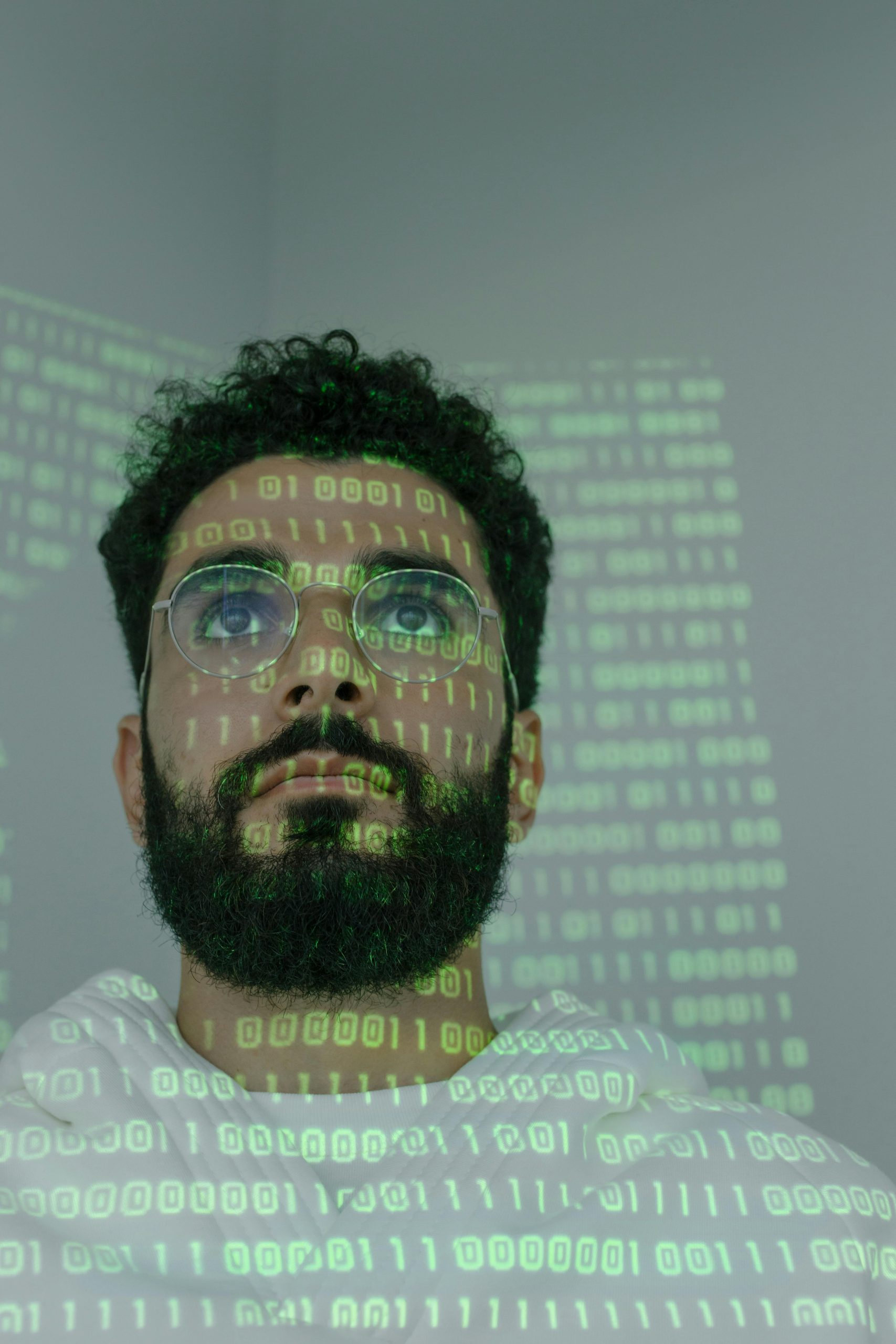 A bearded man with eyeglasses analyzing data in a digital environment with green binary code projections.